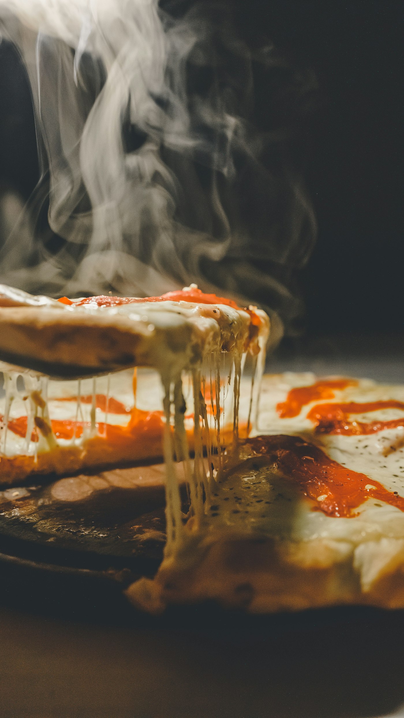 A wood-fired pizza being lifted, melted cheese stretching as steam rises